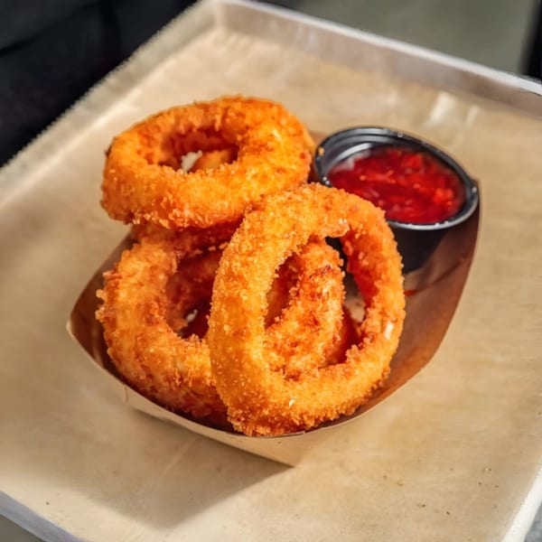 Crispy golden onion rings from Tampa Burger Company, served with a side of red dipping sauce.