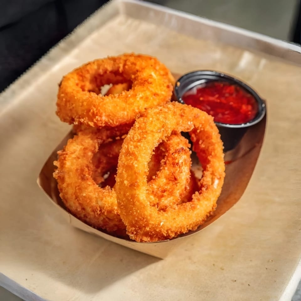 Crispy golden onion rings from Tampa Burger Company, served with a side of red dipping sauce.