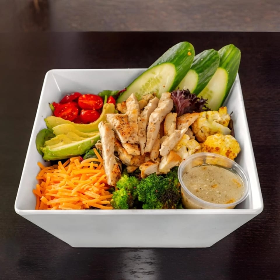 A fresh chicken salad with avocado, tomatoes, cucumbers, broccoli, and shredded carrots.