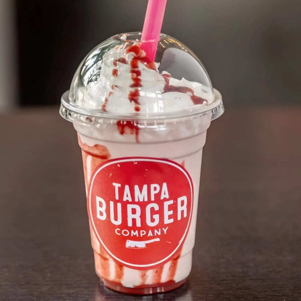 A Tampa Burger Company strawberry milkshake with whipped cream, strawberry drizzle, and a pink straw.