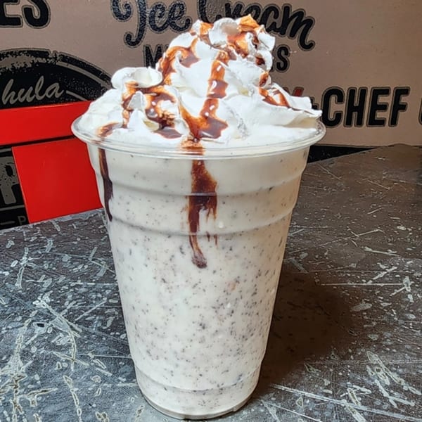 Oreo milkshake with whipped cream and chocolate drizzle in a clear plastic cup.