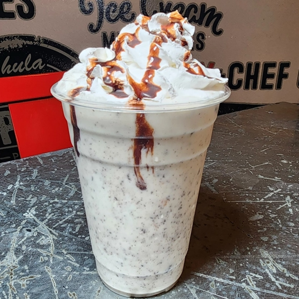 Oreo milkshake with whipped cream and chocolate drizzle in a clear plastic cup.