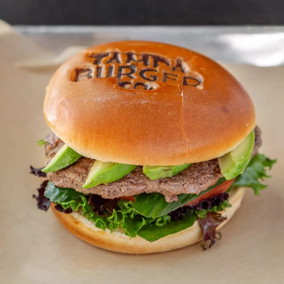 Tampa Burger Co. burger with avocado, lettuce, and tomato on a branded bun.