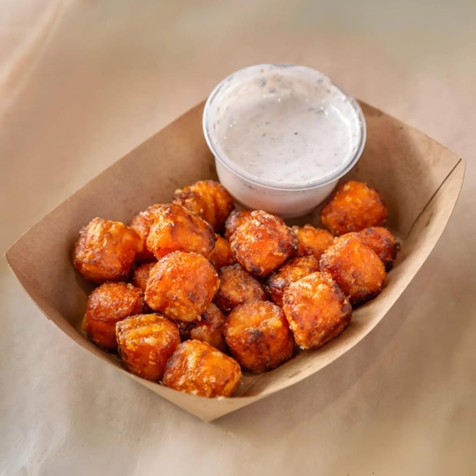 A boat of golden-brown fried cheese curds with a side of ranch dipping sauce.