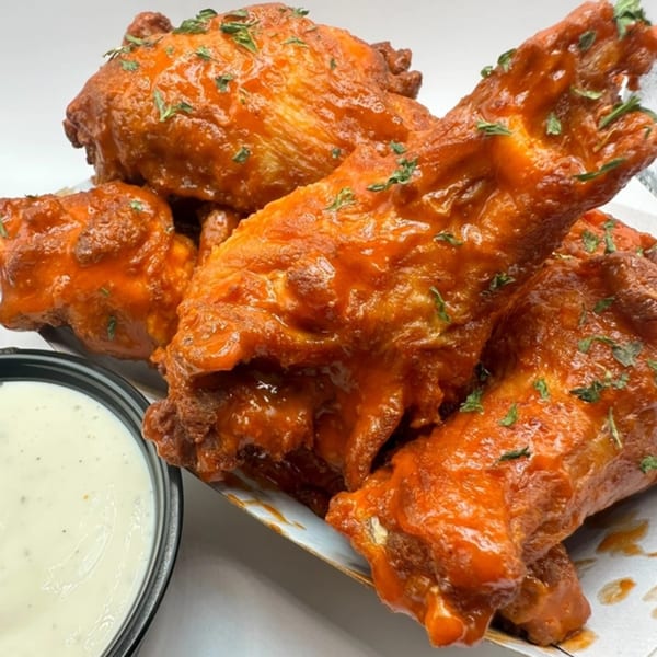 Close-up of five buffalo chicken wings with ranch dressing on the side.