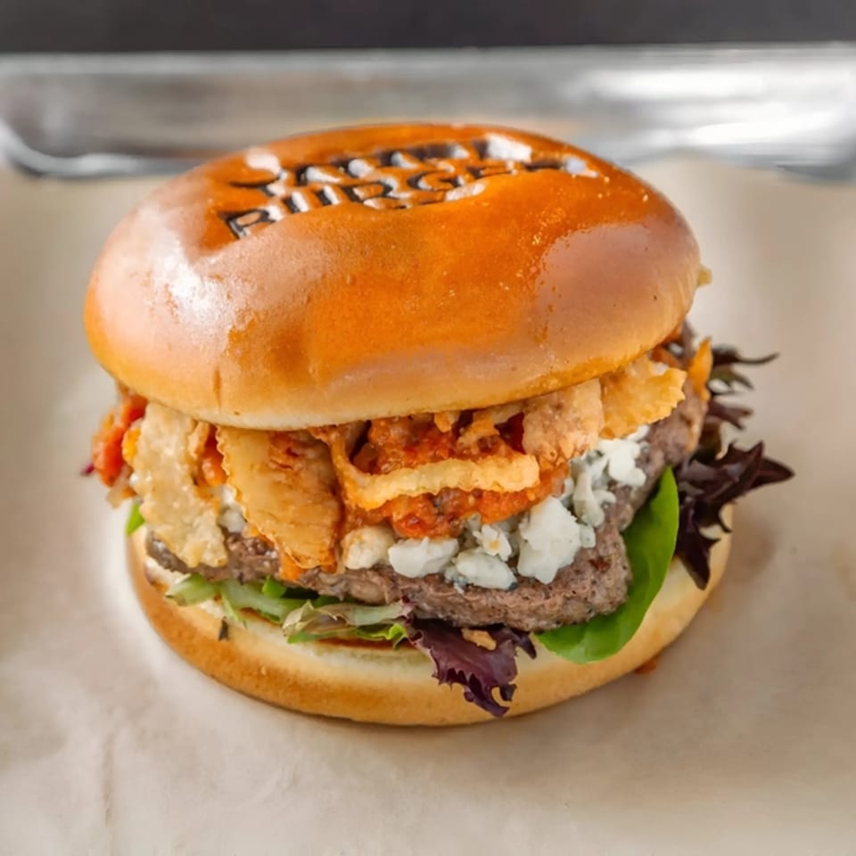 Tampa Burger Company burger with blue cheese, fried onions, and lettuce on a branded bun.